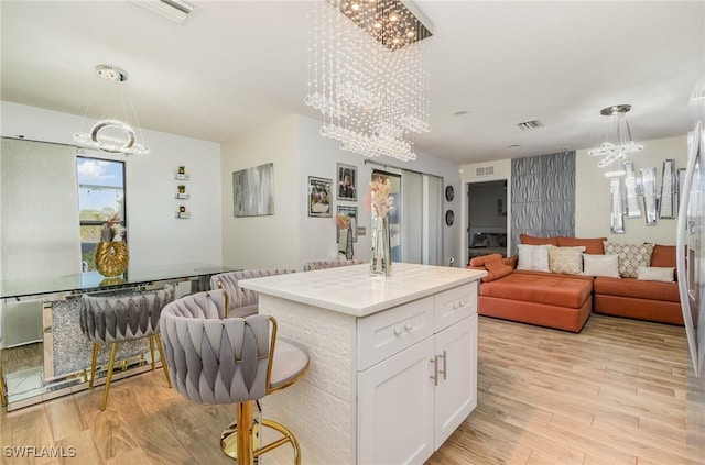 kitchen with a center island, a chandelier, decorative light fixtures, light hardwood / wood-style floors, and white cabinets