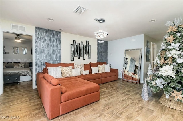 living room with ceiling fan with notable chandelier and light hardwood / wood-style flooring