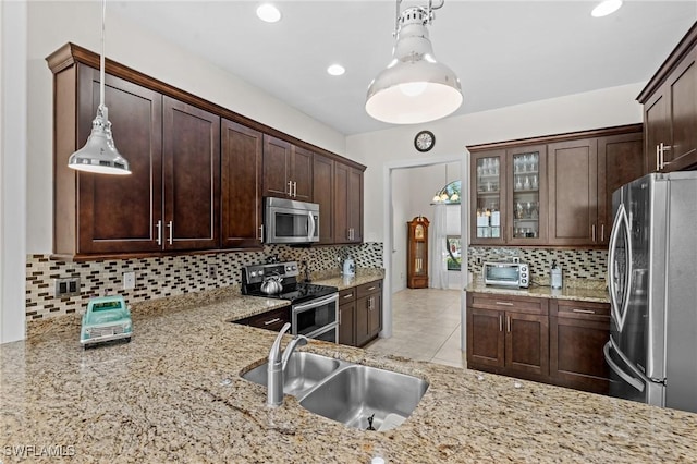 kitchen featuring pendant lighting, sink, dark brown cabinets, stainless steel appliances, and light stone counters