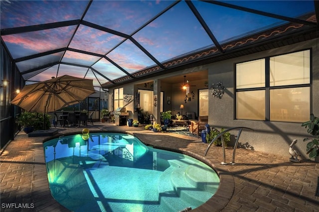 pool at dusk with ceiling fan, a lanai, and a patio area