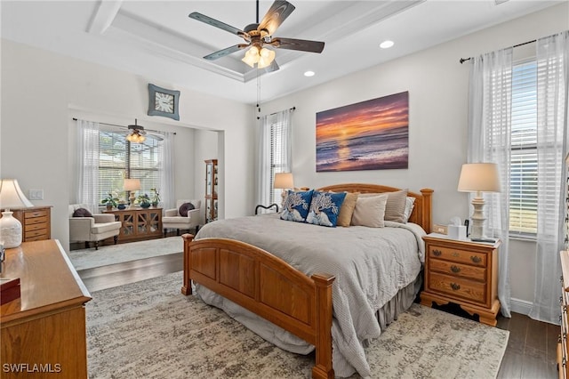 bedroom featuring multiple windows, dark wood-type flooring, ceiling fan, and a tray ceiling