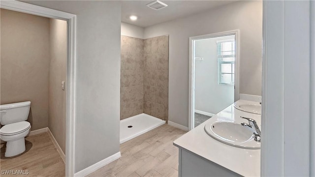 bathroom with tiled shower, hardwood / wood-style floors, vanity, and toilet