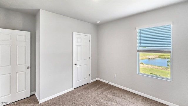 unfurnished bedroom featuring dark colored carpet, a water view, and multiple windows