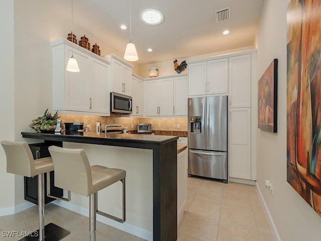 kitchen with kitchen peninsula, stainless steel appliances, white cabinets, hanging light fixtures, and a breakfast bar area