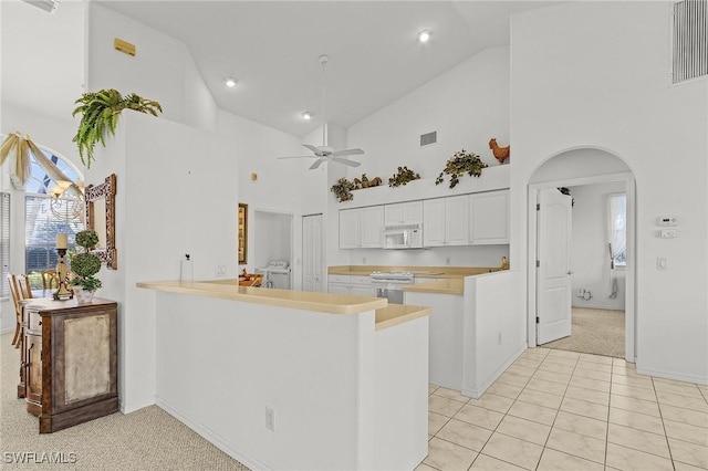 kitchen featuring kitchen peninsula, stove, ceiling fan, high vaulted ceiling, and white cabinetry