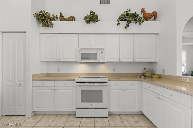 kitchen featuring white cabinets, light tile patterned flooring, and white appliances