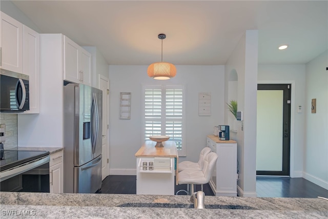 kitchen with white cabinets, appliances with stainless steel finishes, decorative light fixtures, and light stone countertops