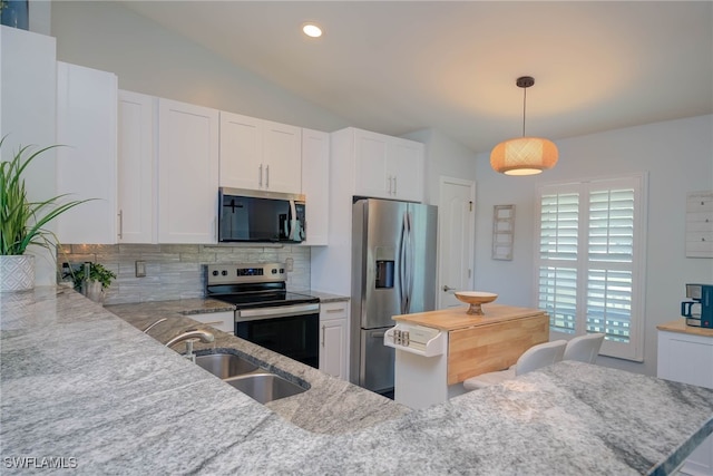 kitchen featuring lofted ceiling, white cabinetry, hanging light fixtures, and appliances with stainless steel finishes