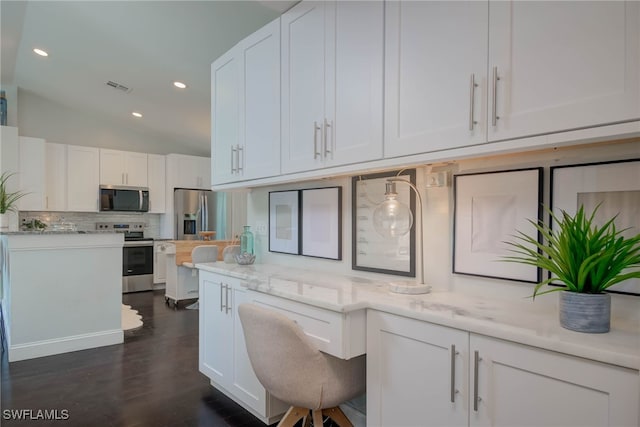 kitchen featuring lofted ceiling, backsplash, appliances with stainless steel finishes, light stone counters, and white cabinetry