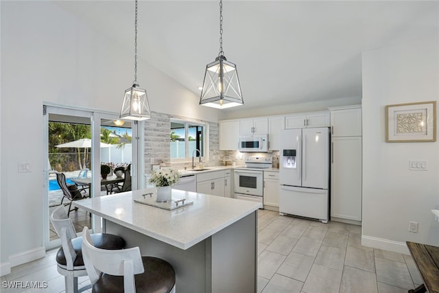 kitchen featuring white appliances, vaulted ceiling, sink, white cabinetry, and hanging light fixtures