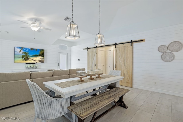 tiled dining area with wood walls, ceiling fan, a barn door, and high vaulted ceiling