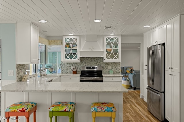 kitchen featuring kitchen peninsula, premium range hood, light stone counters, stainless steel appliances, and white cabinets