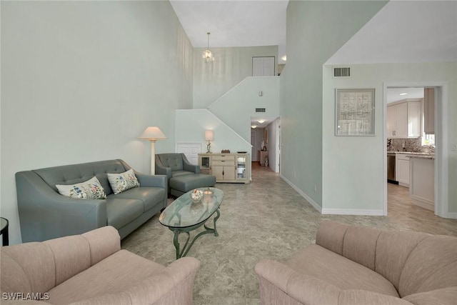 living room featuring visible vents, a notable chandelier, a towering ceiling, and baseboards