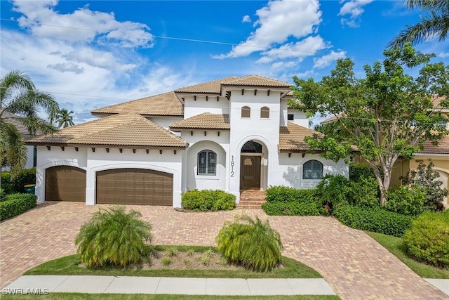 mediterranean / spanish house featuring an attached garage, a tiled roof, decorative driveway, and stucco siding