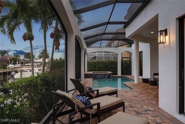 pool at dusk featuring an in ground hot tub, glass enclosure, and a patio area