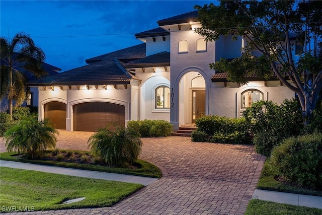 mediterranean / spanish-style home featuring an attached garage, driveway, a tile roof, and stucco siding