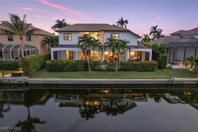 back house at dusk featuring a yard and a water view