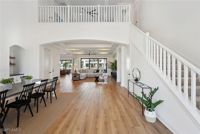 interior space with a high ceiling, coffered ceiling, ceiling fan, light wood-type flooring, and beamed ceiling