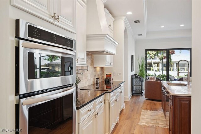 kitchen featuring sink, light hardwood / wood-style flooring, double oven, premium range hood, and black electric stovetop