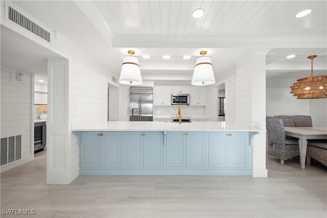 kitchen with kitchen peninsula, decorative light fixtures, stainless steel appliances, and light hardwood / wood-style floors