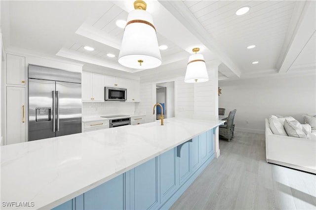 kitchen with light stone counters, sink, built in appliances, decorative light fixtures, and white cabinets