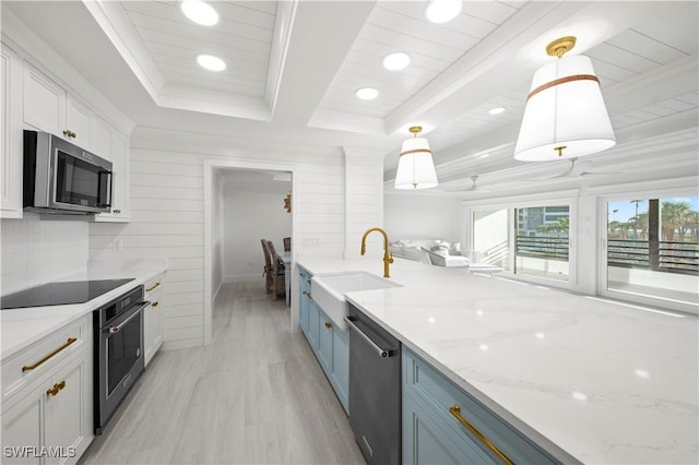 kitchen featuring light stone countertops, white cabinetry, sink, stainless steel appliances, and pendant lighting