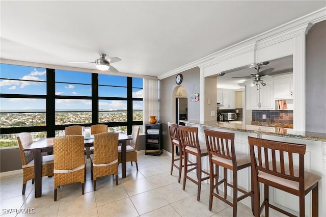 tiled dining space with ceiling fan, a wall of windows, and ornamental molding