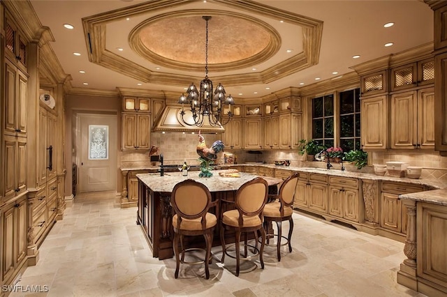 kitchen with light stone countertops, a raised ceiling, hanging light fixtures, and an island with sink