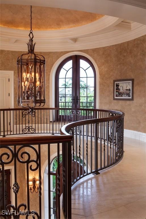 stairs with a raised ceiling, french doors, ornamental molding, and an inviting chandelier