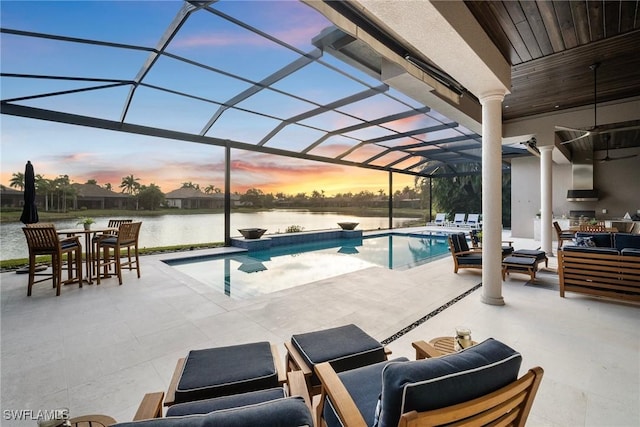 pool at dusk with a lanai, a water view, a patio area, and outdoor lounge area