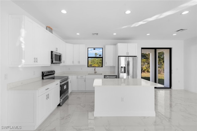 kitchen with appliances with stainless steel finishes, sink, white cabinetry, and a kitchen island