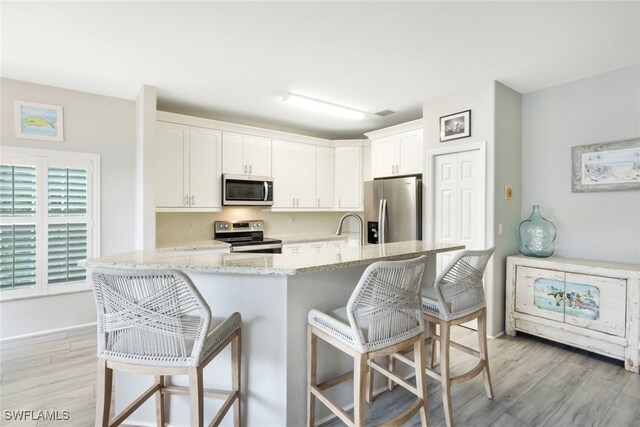 kitchen featuring a kitchen breakfast bar, light wood-type flooring, light stone counters, stainless steel appliances, and white cabinetry