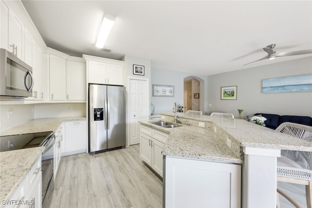 kitchen with a center island with sink, a ceiling fan, a sink, arched walkways, and appliances with stainless steel finishes