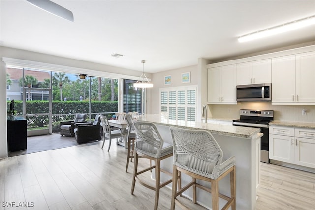 kitchen with decorative backsplash, appliances with stainless steel finishes, light stone countertops, pendant lighting, and white cabinets