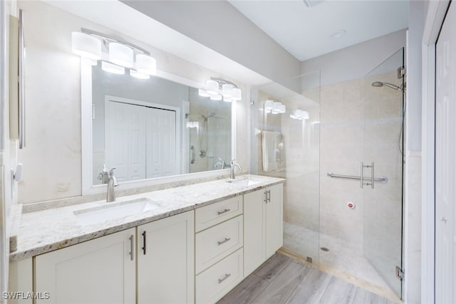 bathroom with a shower stall, wood finished floors, double vanity, and a sink