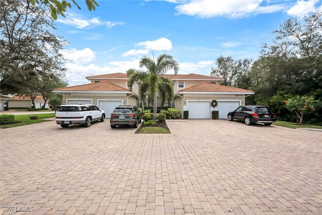 view of front facade with a garage, decorative driveway, a tile roof, and stucco siding