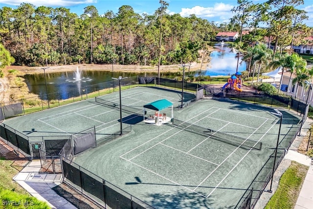 view of tennis court featuring playground community, a water view, and fence