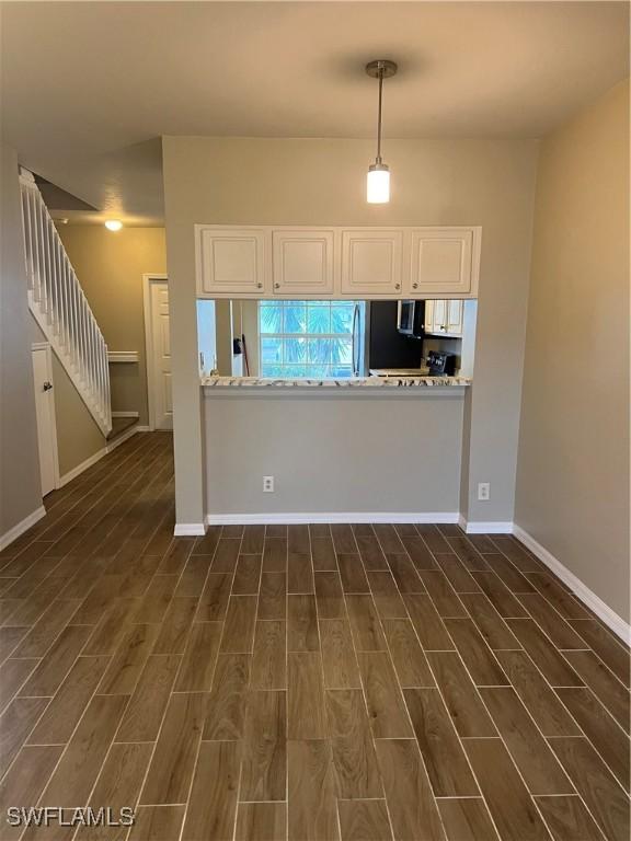 kitchen with pendant lighting, kitchen peninsula, light stone countertops, dark hardwood / wood-style flooring, and white cabinetry