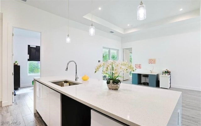 kitchen featuring a center island with sink, a raised ceiling, sink, decorative light fixtures, and white cabinetry