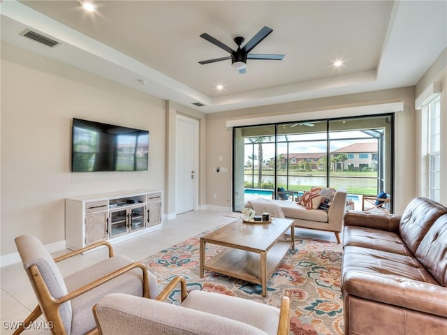 tiled living room featuring a tray ceiling, ceiling fan, and a healthy amount of sunlight