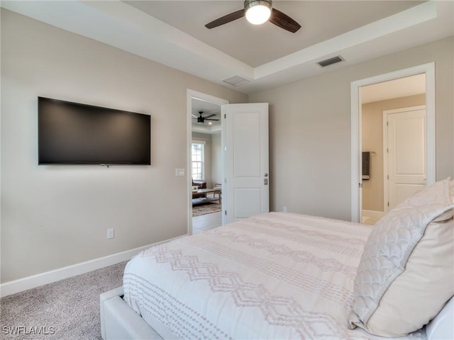 carpeted bedroom with ceiling fan, a tray ceiling, and ensuite bath