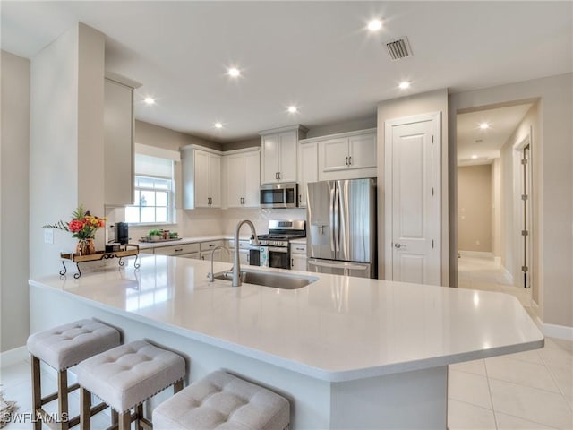 kitchen featuring sink, kitchen peninsula, a breakfast bar area, light tile patterned floors, and appliances with stainless steel finishes