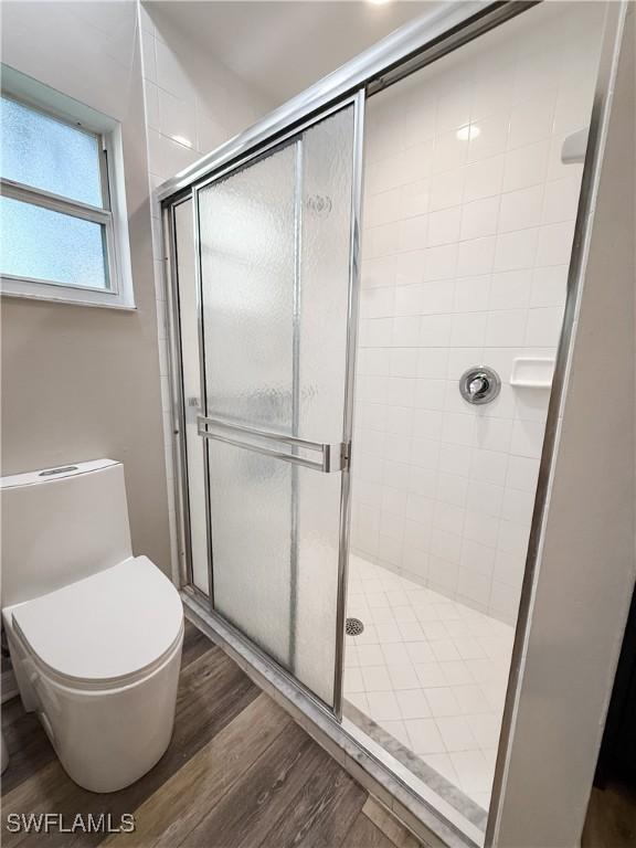 bathroom featuring wood-type flooring, a shower with shower door, and toilet