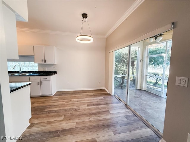 kitchen featuring crown molding, sink, decorative light fixtures, light hardwood / wood-style floors, and white cabinetry