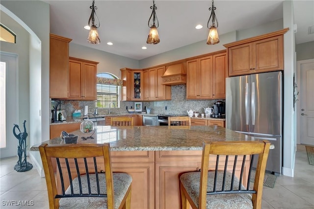 kitchen with sink, hanging light fixtures, light stone counters, appliances with stainless steel finishes, and custom exhaust hood