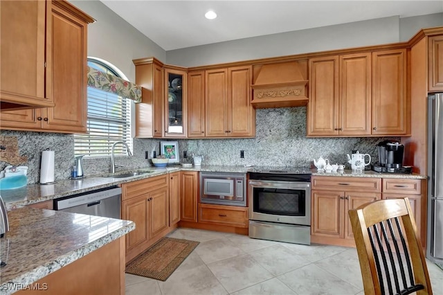 kitchen with backsplash, premium range hood, sink, light stone counters, and stainless steel appliances