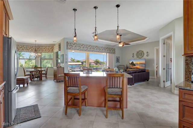 kitchen with a breakfast bar, a tray ceiling, stainless steel refrigerator, and plenty of natural light