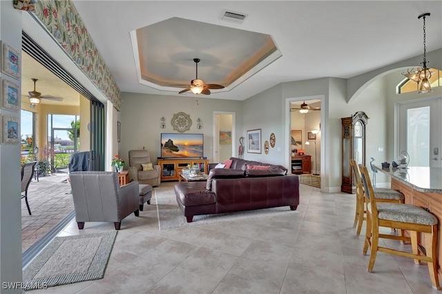 living room featuring a tray ceiling and ceiling fan with notable chandelier