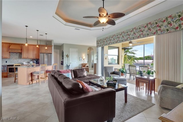 living room featuring ceiling fan, light tile patterned floors, and a tray ceiling