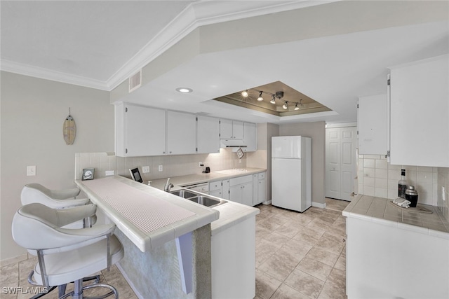 kitchen featuring kitchen peninsula, a tray ceiling, sink, white cabinets, and white fridge